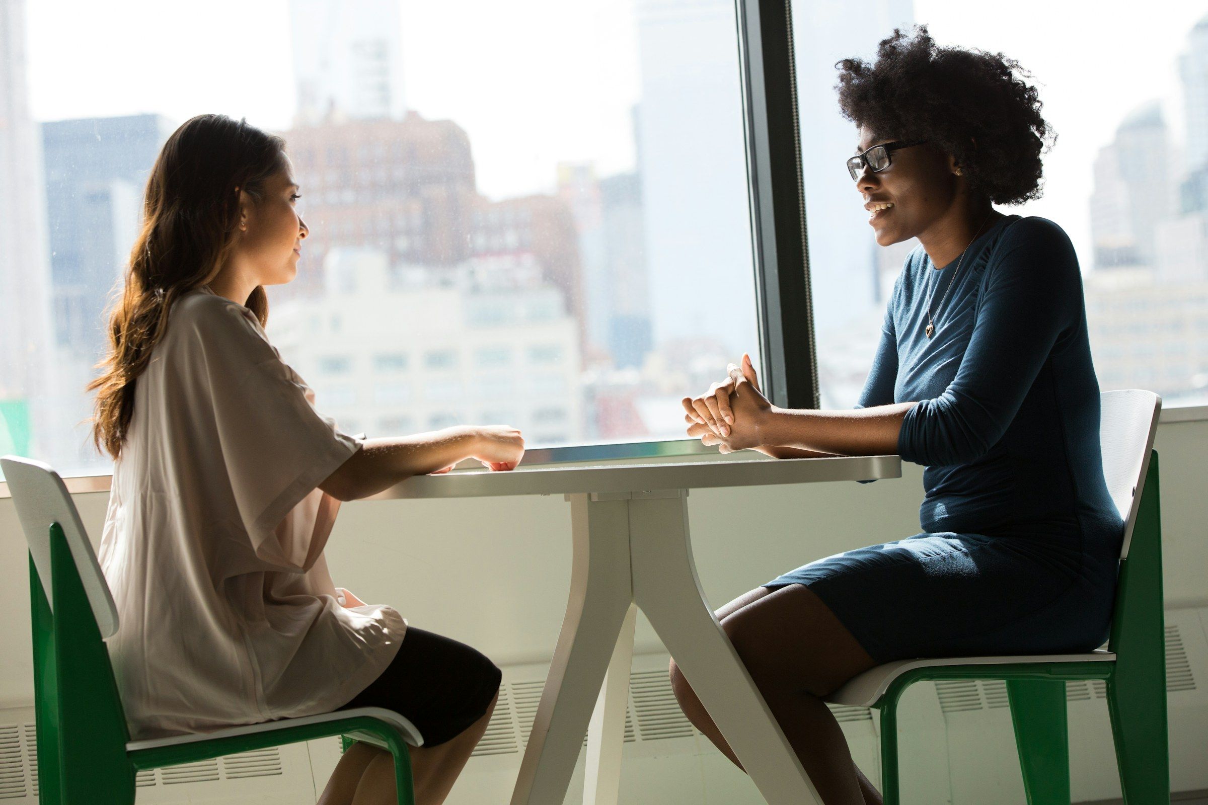 Two women seated across a table in conversation beside a bright window